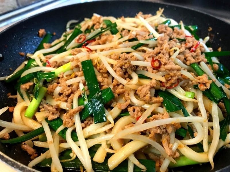 フライパンで冷凍うどん、豚ひき肉、ニラ、もやしを調味料と炒め合わせている様子