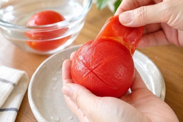 トマトの塩昆布和え用に、湯むきしたトマトの皮をやさしく剥いている様子