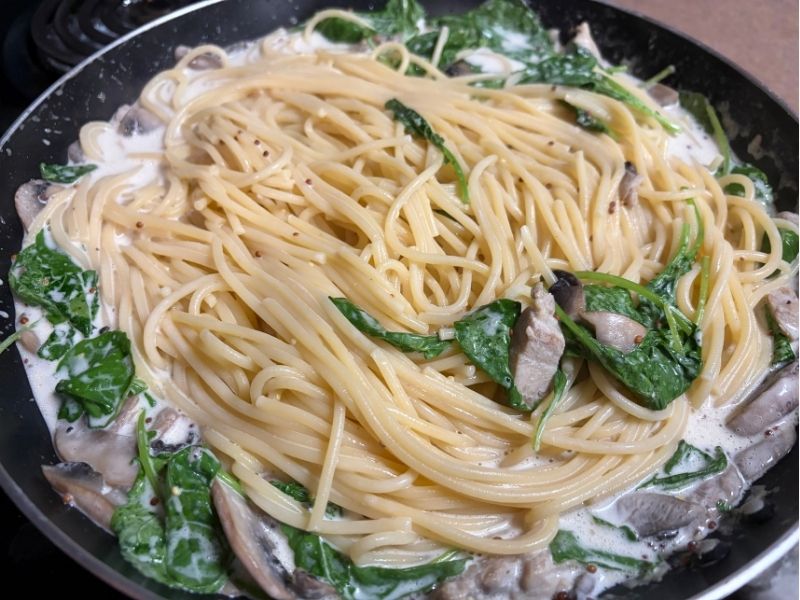 茹でたパスタを鶏肉とマッシュルームの粒マスタードクリームソースに加えて絡める工程