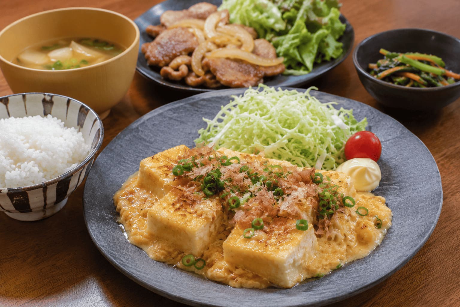 長芋のふわとろ豆腐ステーキに、ご飯、味噌汁、豚肉のおかず、青菜の副菜を添えた食べ応えのある献立の画像