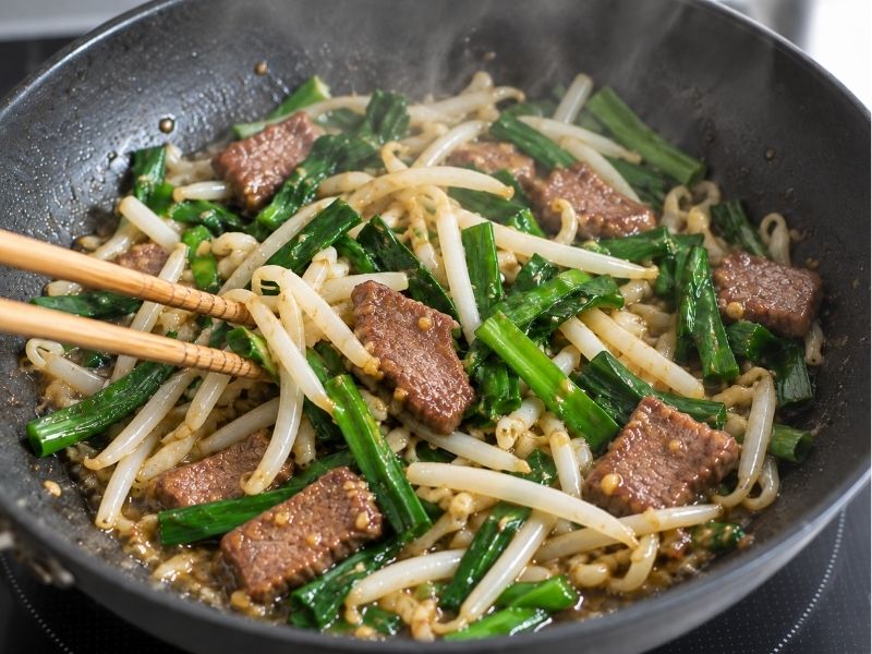 牛タンとニラ、もやしをフライパンで炒めて味付けする調理工程