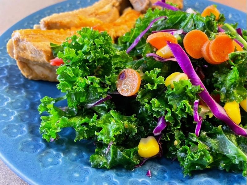 青い皿に盛り付けたケール、紫キャベツ、にんじん、コーンのイタリアンドレッシングサラダ